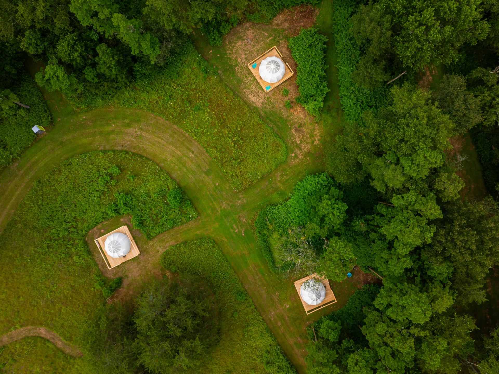 An aerial drone shot of three bell shaped tents surrounded by lush green foliage